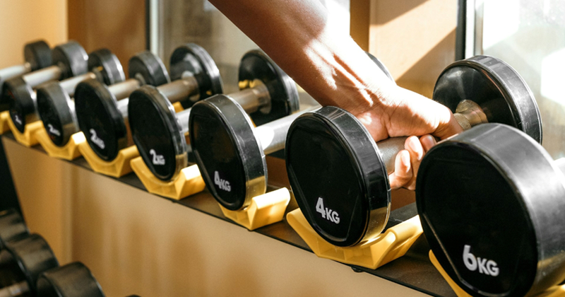 A person taking a 4kg dumbbell off a dumbbell rack