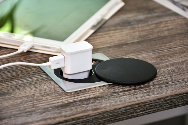 Phone charger plugged into a power outlet beside a tablet on a wooden desk