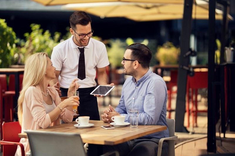 Waiter smiles at couple who are having an anniversary meal.