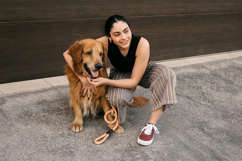 A woman kneels down to take a picture with her golden retriever on the sidewalk