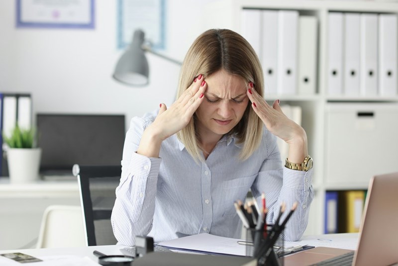 A tired woman holds her fingers to her temples at the office