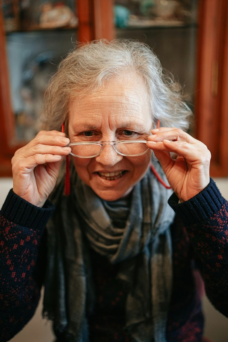 An older woman holds her eyeglasses to her face.