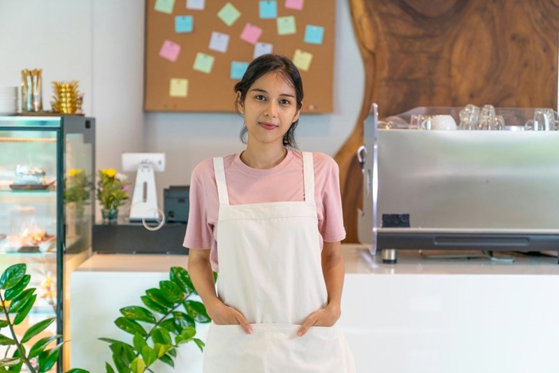 A female employee wearing a kitchen apron stands behind the counter of a breakfast establishment.