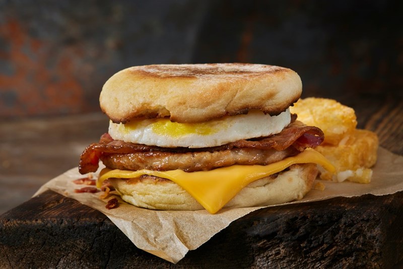 A breakfast burger with eggs, bacon, and cheese sits on a piece of parchment paper.