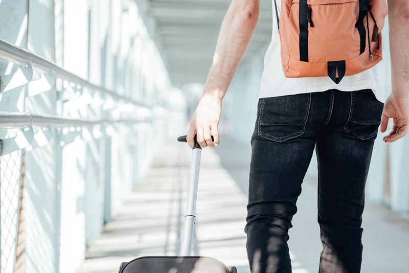 Young traveler walking through an airport corridor with suitcase and backpack.