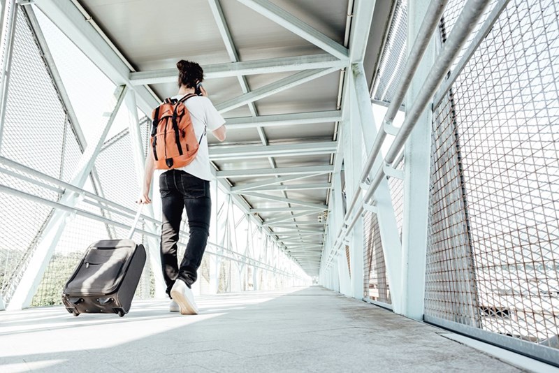 Solo backpacker pulling luggage through a modern transit walkway, perfect representation of budget travel, international trips, and youth tourism.