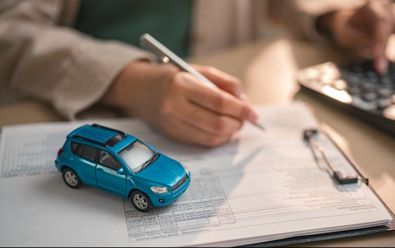 Person signing car insurance or financing documents beside a blue model car and calculator.