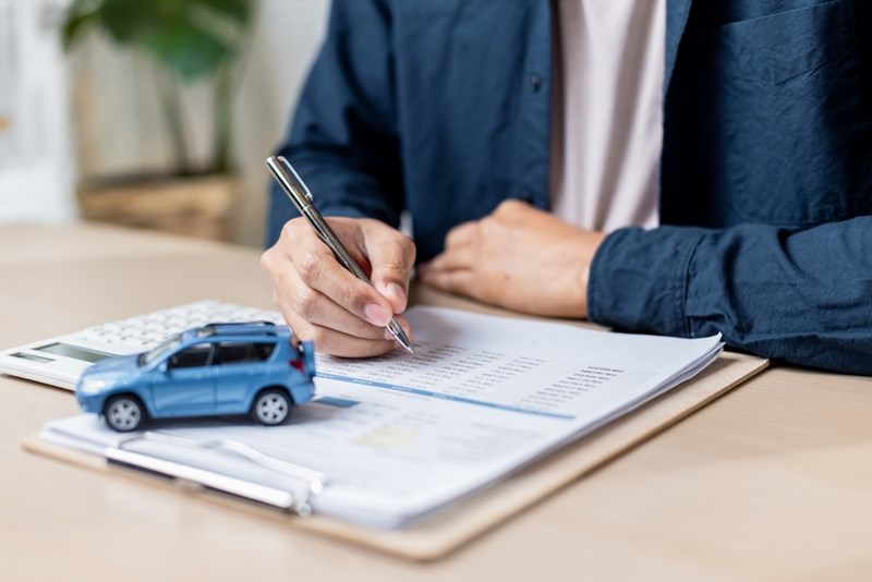 Person completing car insurance or auto loan paperwork beside a blue model SUV and calculator.