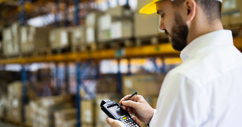 A warehouse worker writes on a handheld device