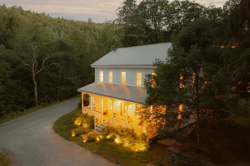 Brightly lit house surrounded by trees and long driveway.