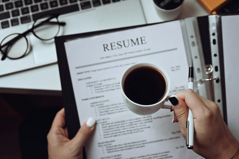 A human resources representative holds a resume in one hands and a coffee mug in the other.