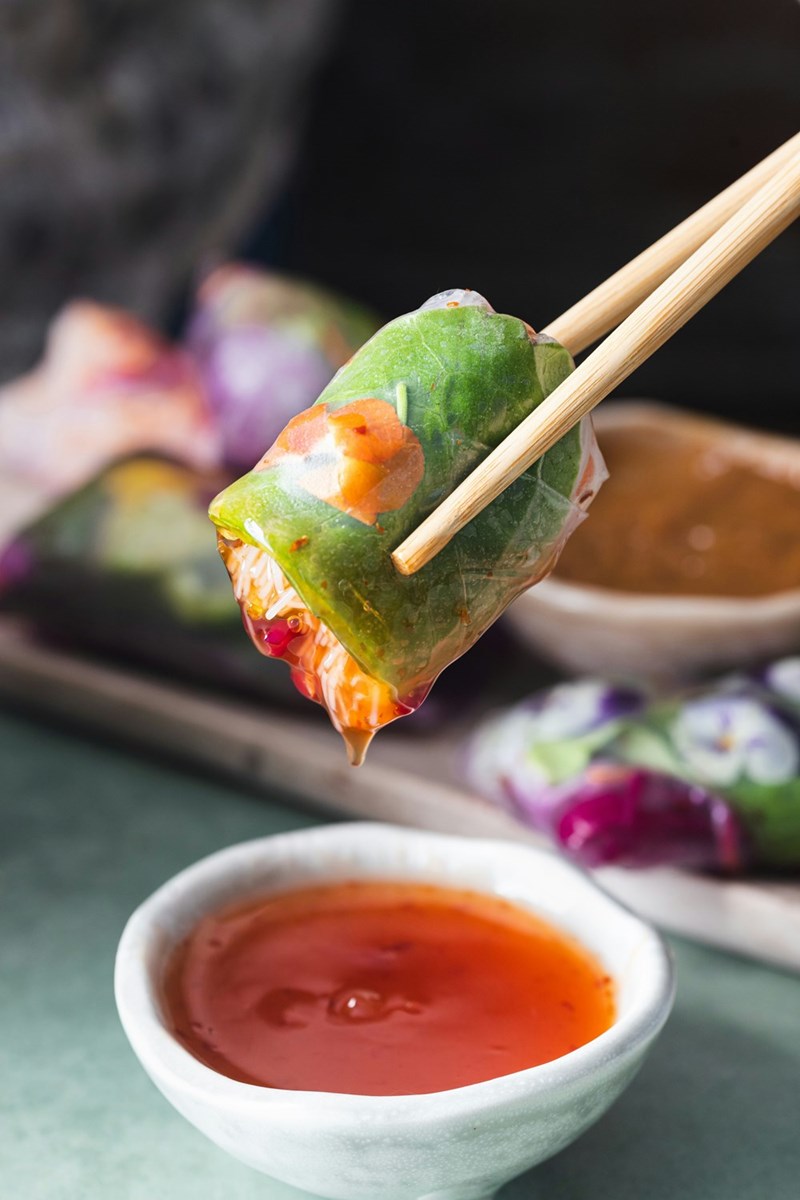 A person holding chopsticks over a bowl of dipping sauce