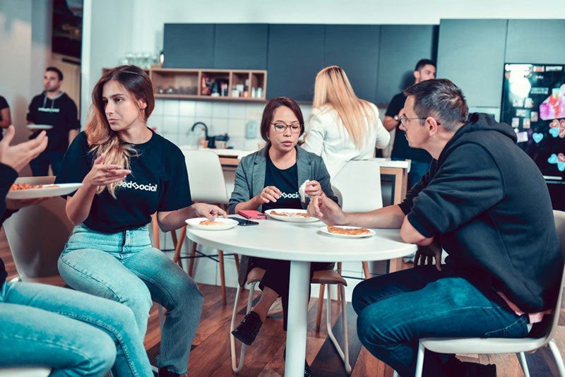 Office kitchen full of employees talking and eating their meals together.
