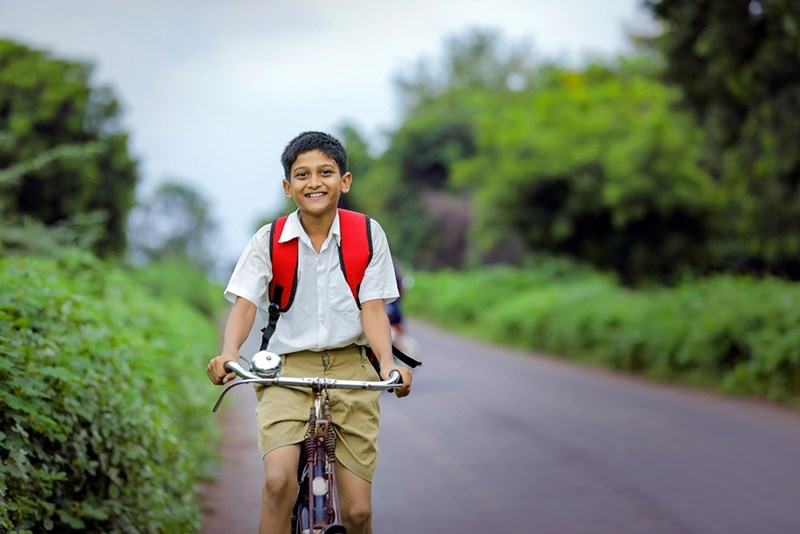 Boy riding a bike on a road wearing school uniform and a backpack.