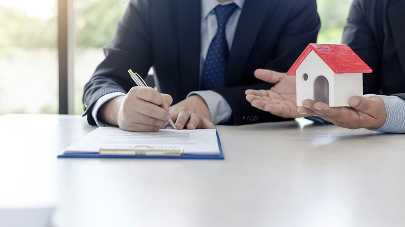A property manager signs a contract as a real estate agent speaks next to him in a conference room.