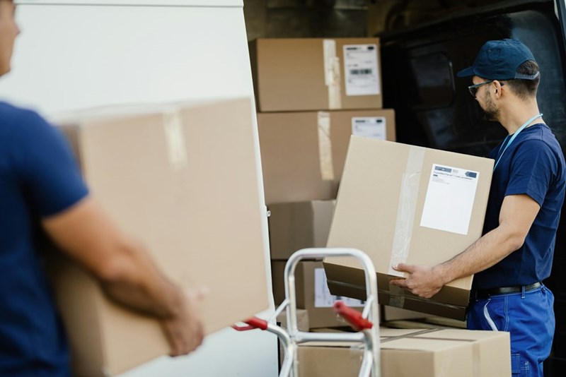 Delivery workers loading cardboard boxes into a moving truck, representing relocation services, job transfers, and long-distance moving logistics.