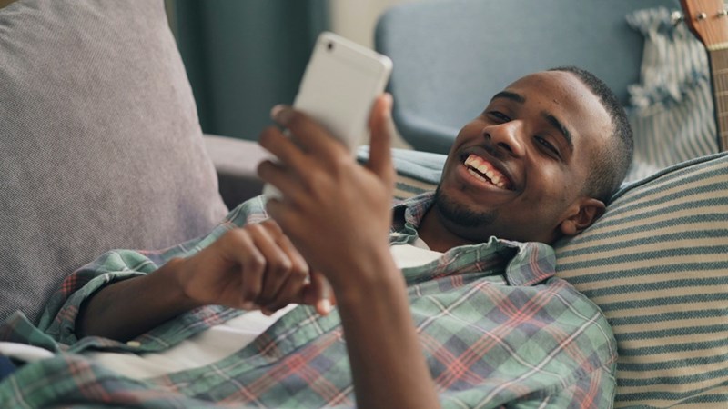 A man laying on a couch holding a smart phone