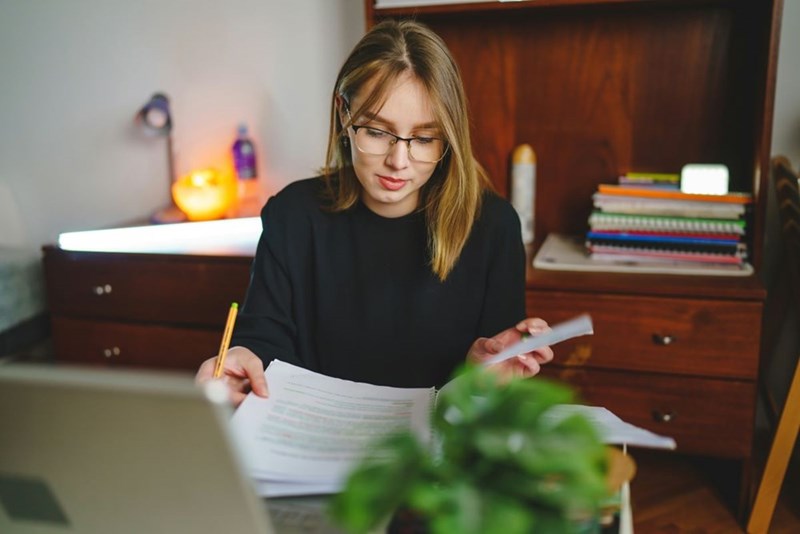 One young caucasian woman sitting at home writing and reading in her notebook holding pencil