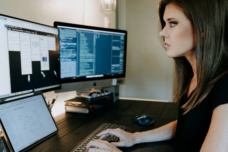 A woman sits at a desk using a computer at home