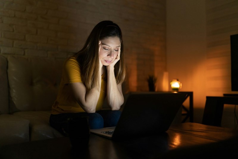 Woman looking stressed while using a laptop at night in a dimly lit living room