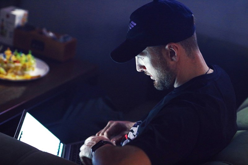 Man using a laptop late at night in a dark room with screen light reflecting on his face.