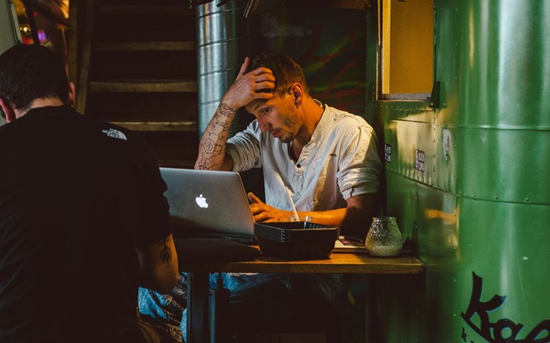 A man looks stressed in front of a macbook in a cafe