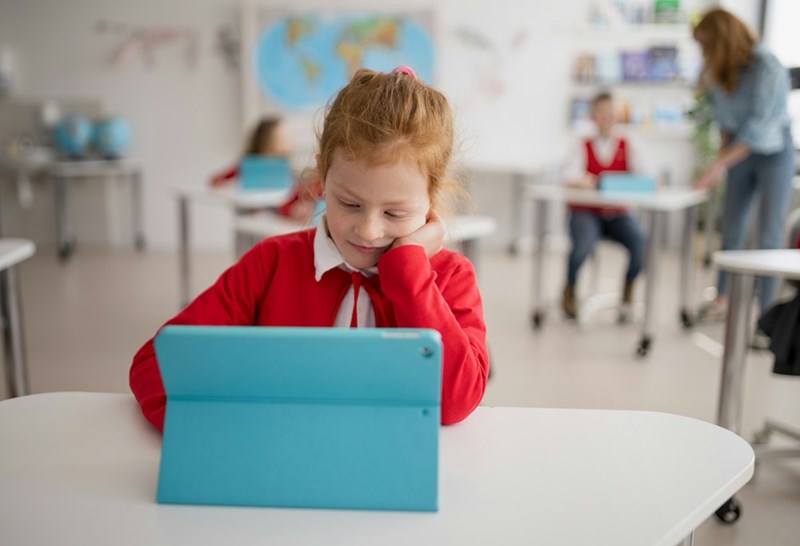 A bored schoolgirl using digital tablet during lesson in classroom at primary school
