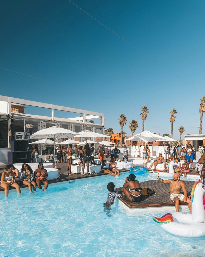 Guests enjoying a lively adults-only pool party under the summer sun with drinks, music, and relaxing vacation vibes.
