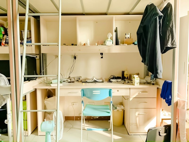 Messy college dorm room with shared furniture and clutter, illustrating chaotic student living conditions and roommate life.