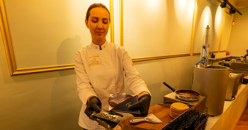 A woman in a white uniform presents a chocolate-coated waffle