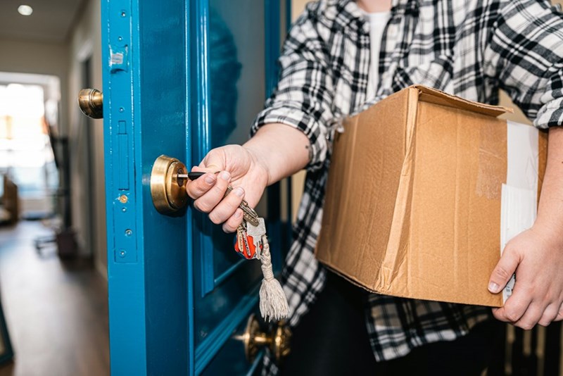 A woman holding a taped-up box while unlocking a door, moving out