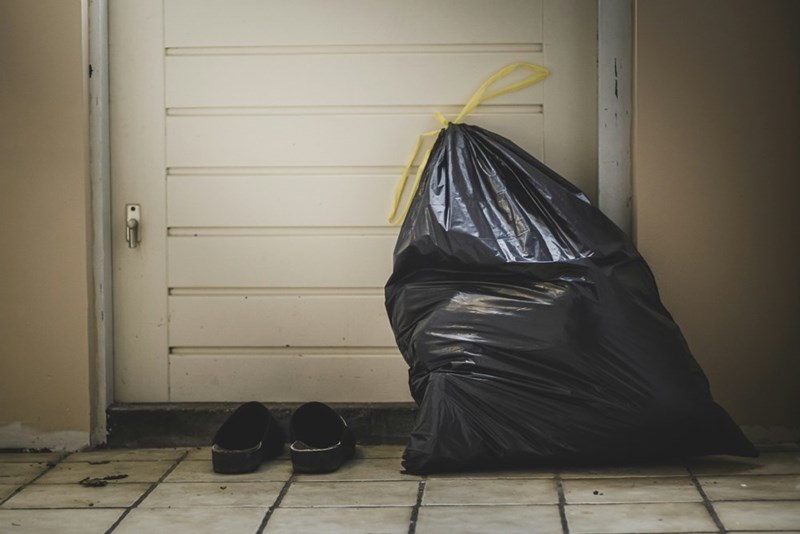 A garbage bag is leaning against a white door with chipped paint