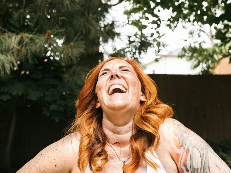 A redheaded woman throws her head back and laughs outside on a sunny day