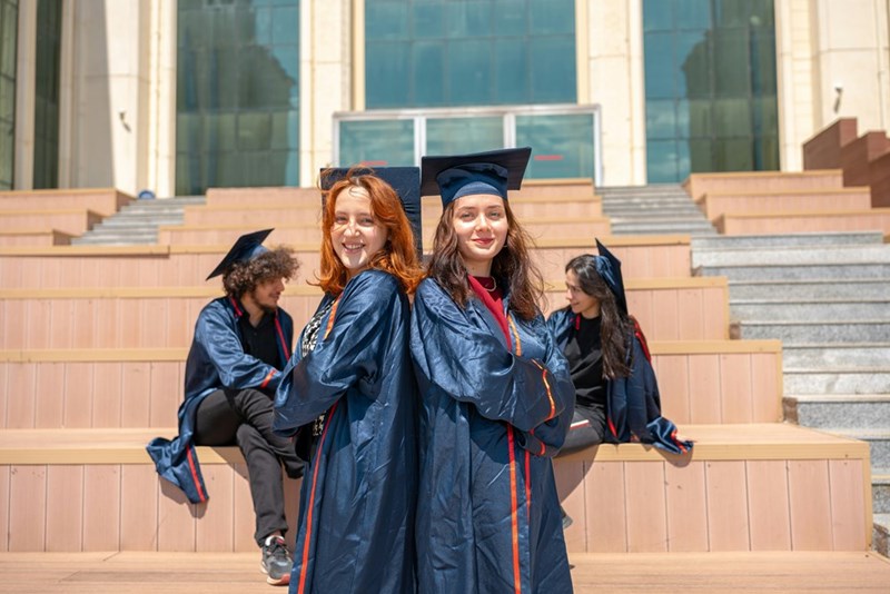A group of four high school students poses on the steps of their school at their graduation.