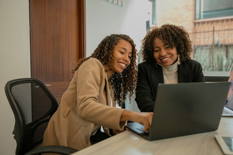 One female employee points something out on her coworker's laptop as she provides advice.