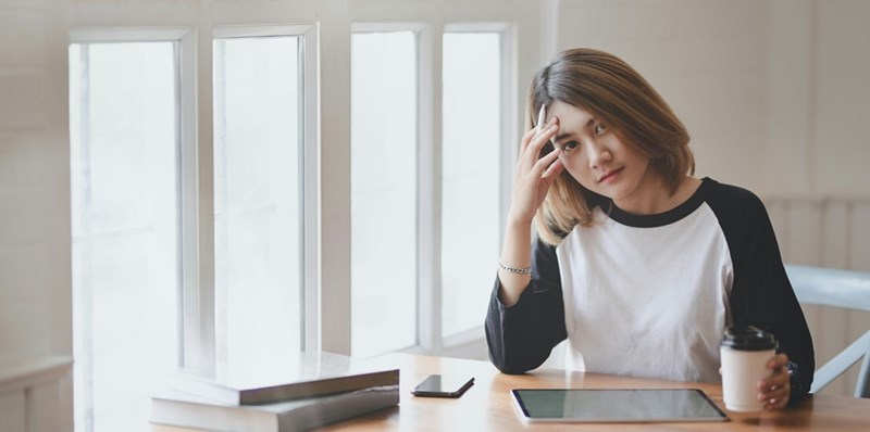 A disappointed female employee puts her head in her hands as she works at her desk.