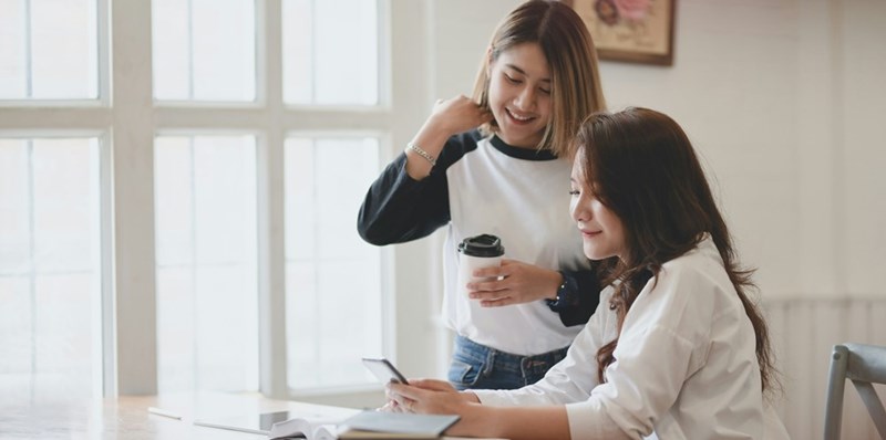 A female employee hovers over her boss's shoulders as she assists her.