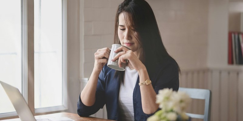 An intense businesswoman sips her coffee while sitting in her private office.
