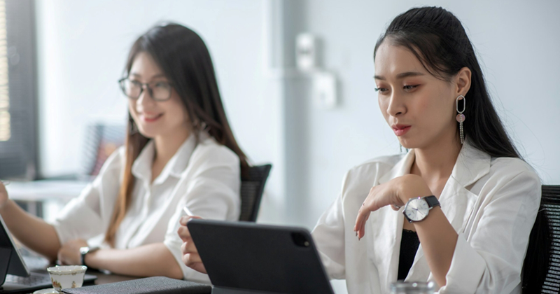 Two female employees sit next to each other and work on tablets