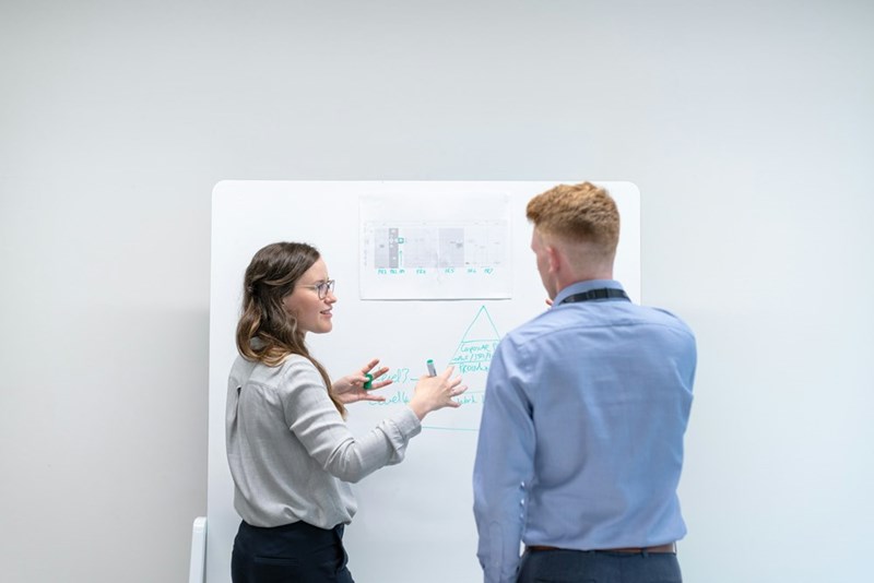 A woman and man are coworkers and are discussing professional ideas in a meeting room using a whiteboard