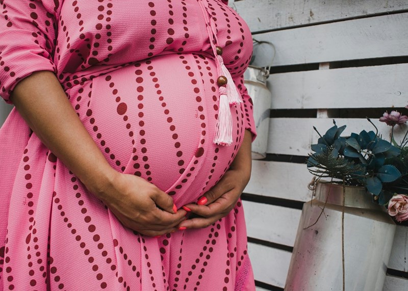 A pregnant woman holds her belly in a pink dress
