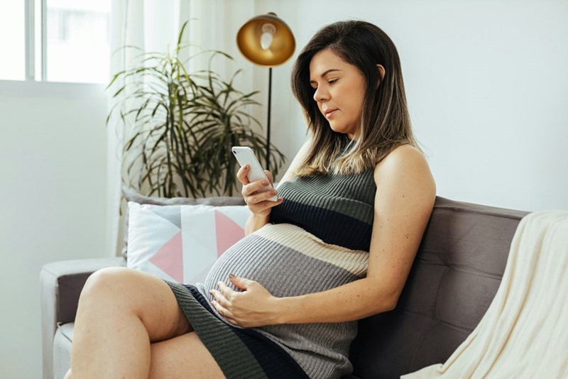 A pregnant woman looks at her phone on her couch