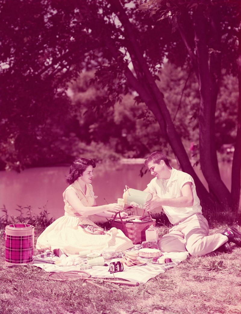Teenage couple having summer picnic by stream circa 1950s in the United States