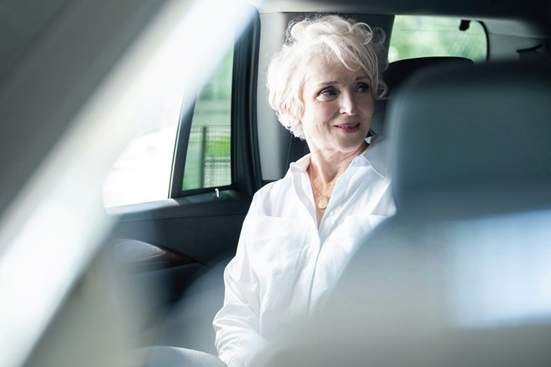 Elder woman sitting in the backseat of a car.