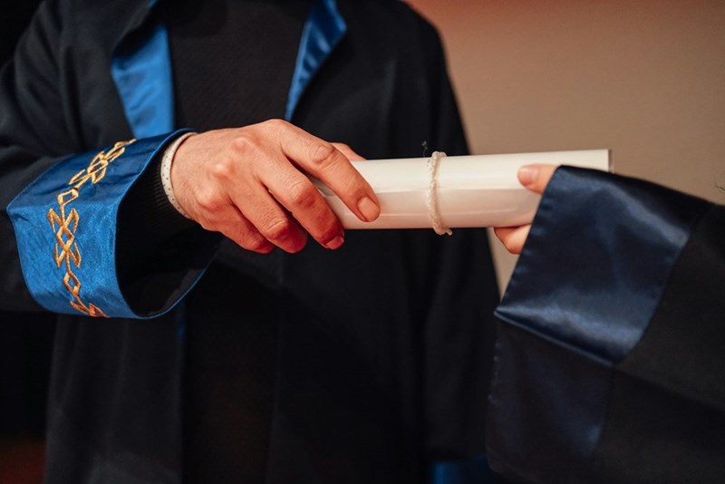 A person in a graduation gown holding a diploma