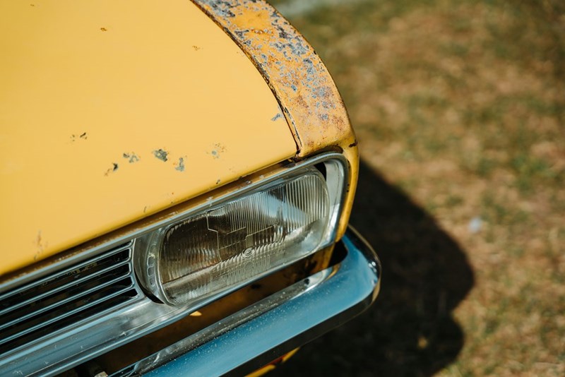 A close-up of an old yellow, rusted classic car body.
