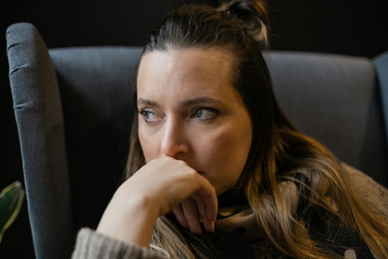 Woman sitting in a chair with her hand against her face, staring off thoughtfully with a worried expression.