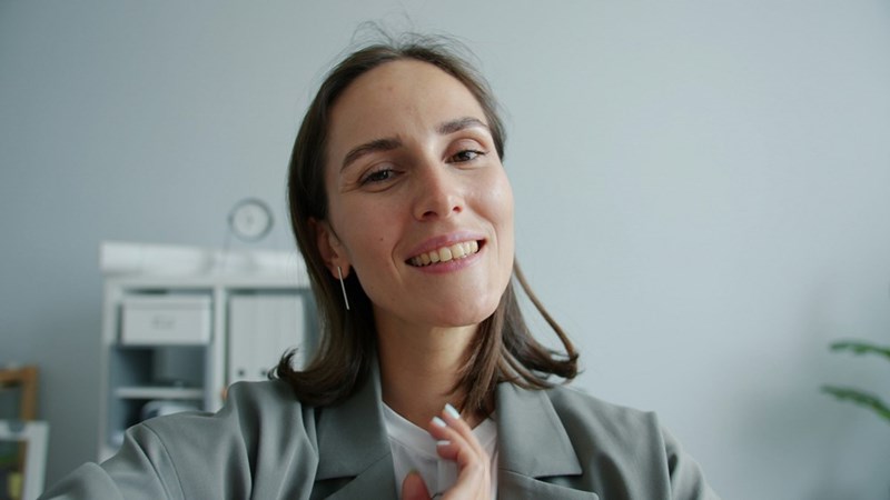 Smiling brunette woman in a blazer posing in a bright modern home office or living room.