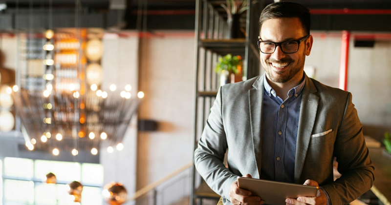A businessman grins while holding a tablet, standing on the mezzanine floor of an office building