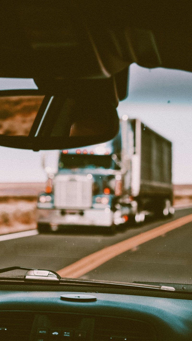 A somewhat blurry photo portrays an artsy portrait from the driver's POV of a large truck driving down the highway